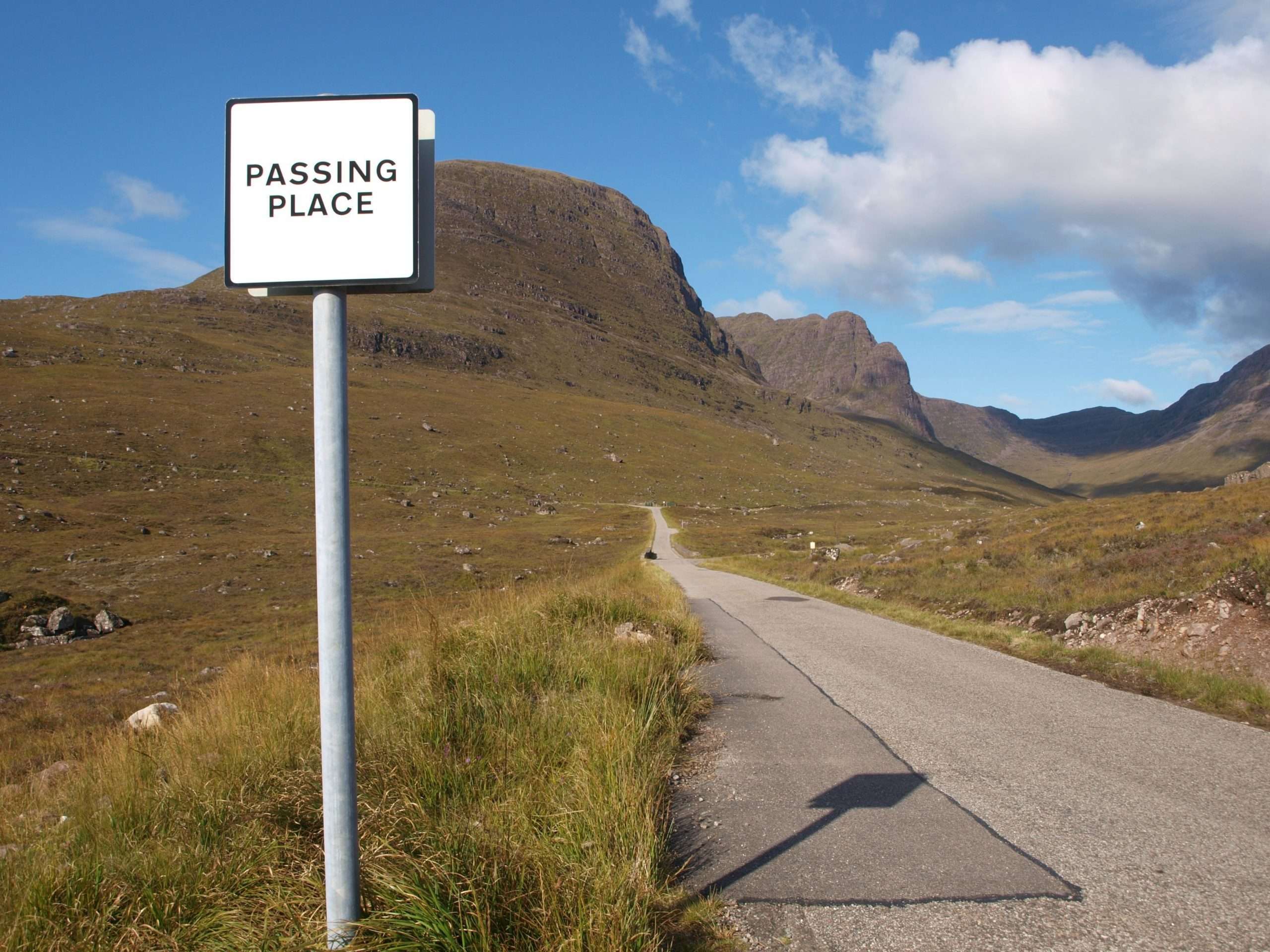A passing place sign is located along the electrified NC500 sustainable campervanning. Sweeping mountain views along the single-track road.